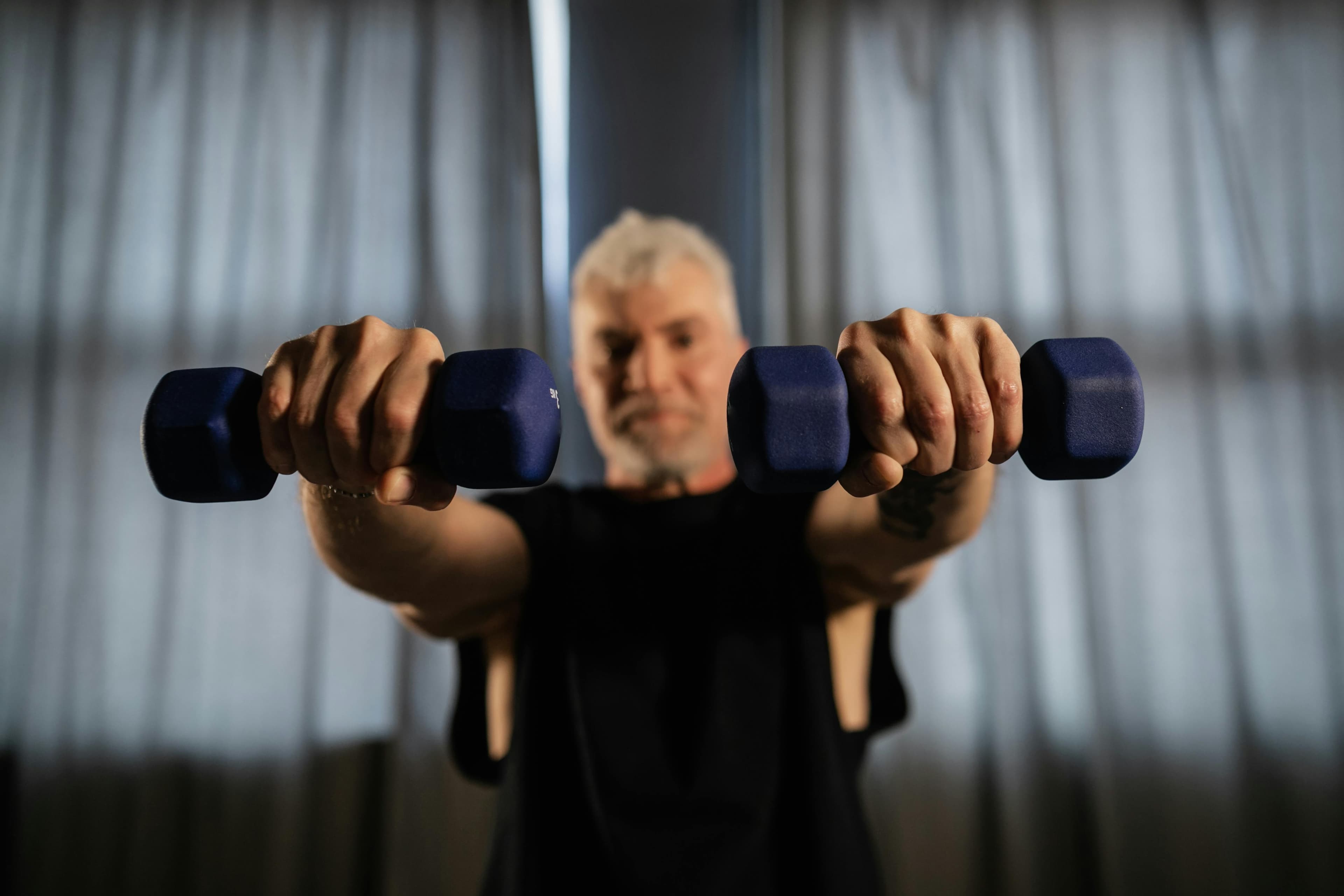 An older man lifting light dumbbells at home