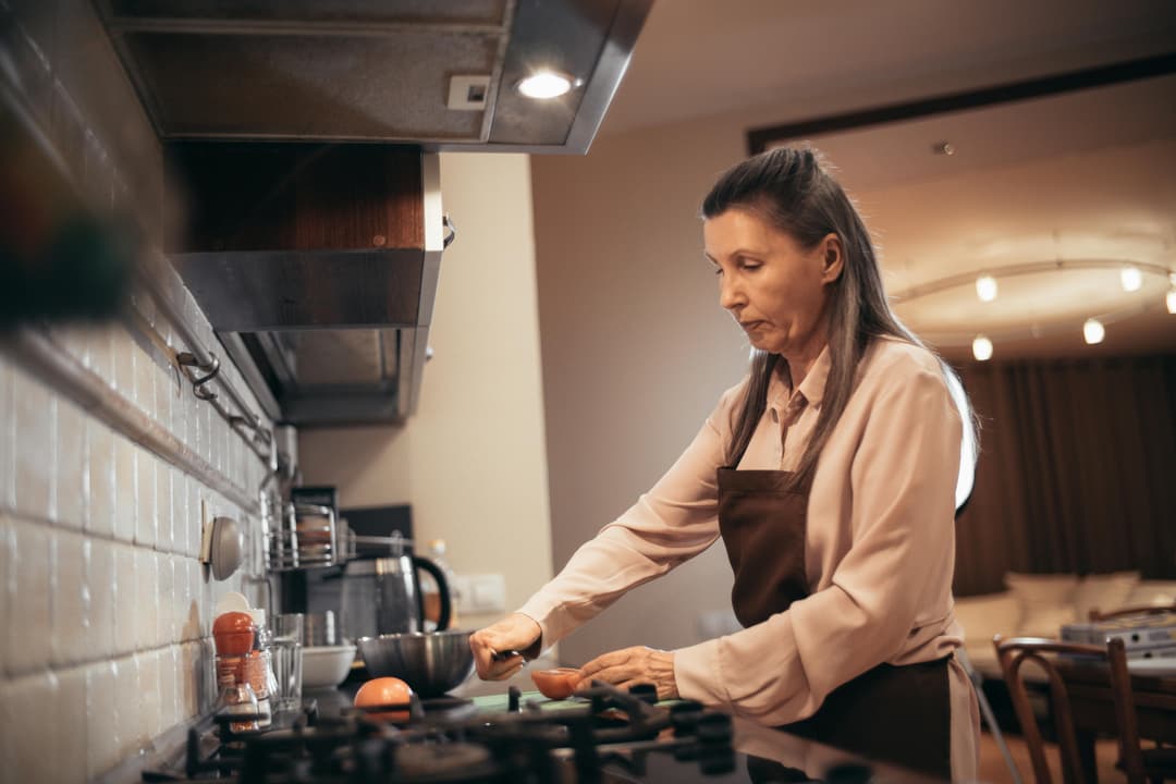 An older woman preparing food at a kitchen stove