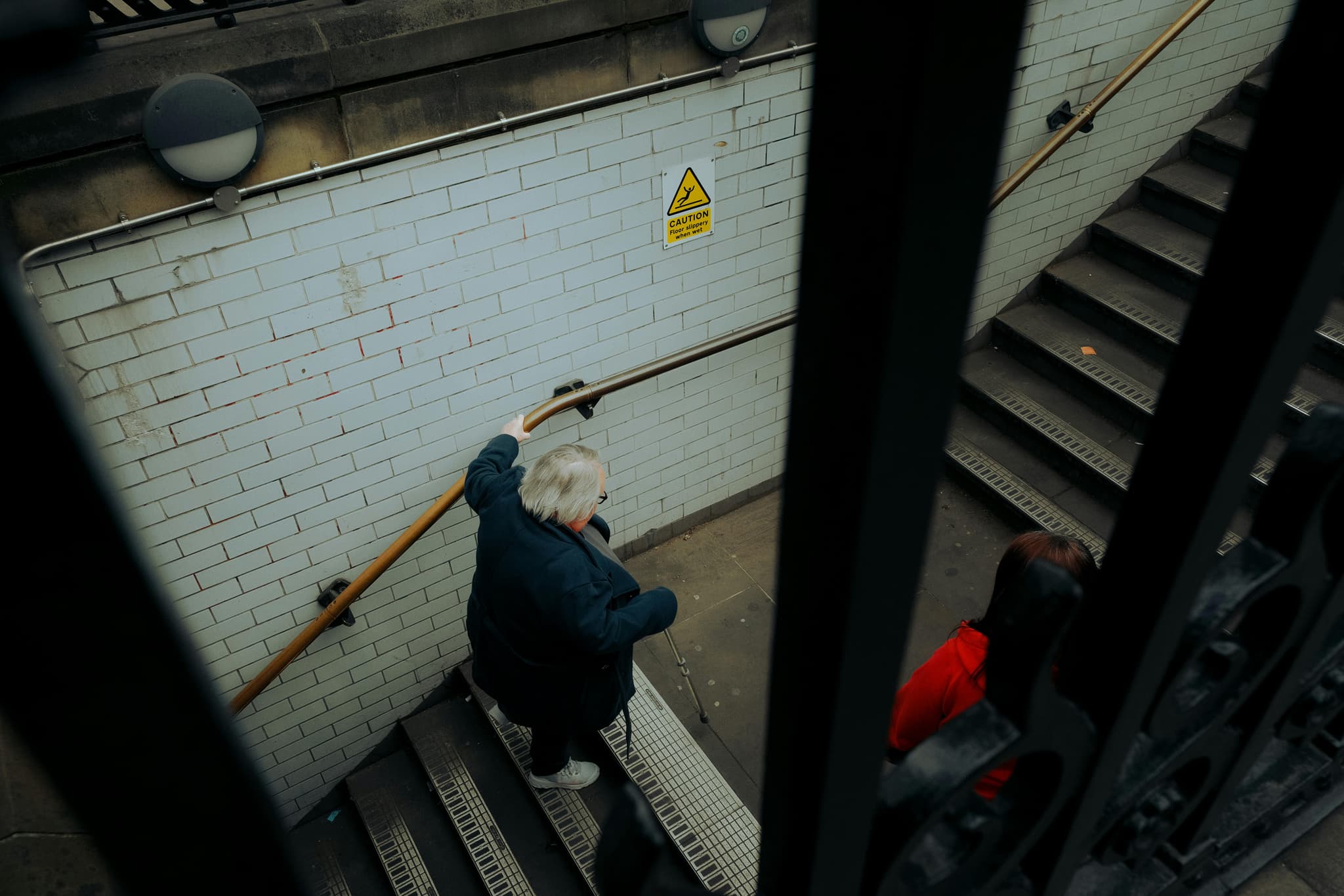 An older woman holding a handrail while navigating subway stairs