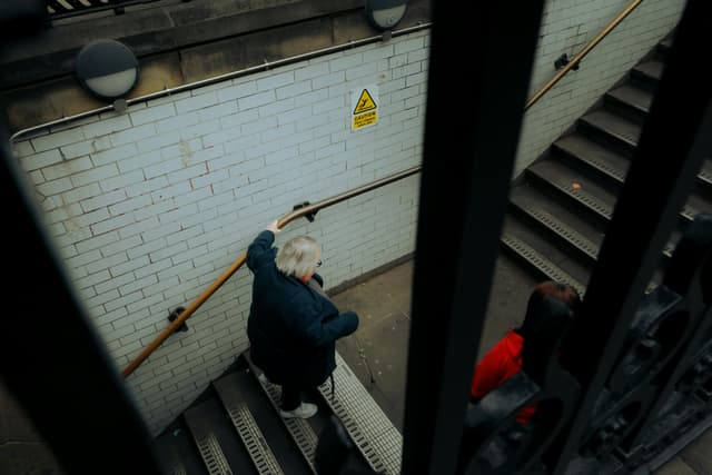An older woman holding a handrail while navigating subway stairs